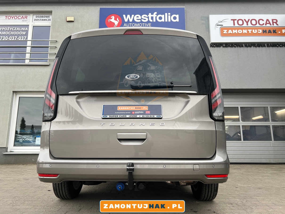 322088600001 na zdjeciu ford tourneo connect z zamontowanym hakiem holowniczym typ stały model f20v za tylnym zderzakiem samochodu na tle bramy warsztatowej